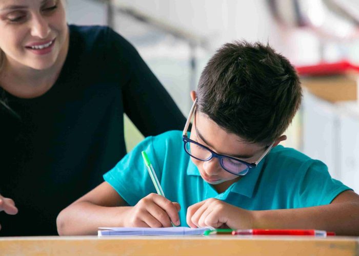 happy-school-teacher-watching-schoolboy-glasses-doing-task-class-1-scaled