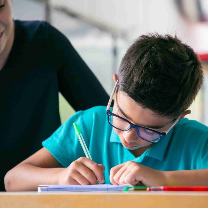 happy-school-teacher-watching-schoolboy-glasses-doing-task-class-1-scaled